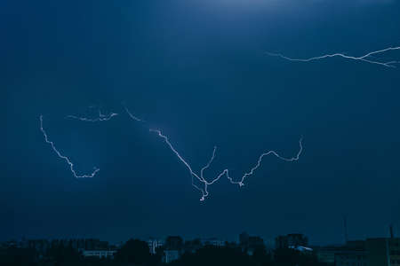 Lightning in sky over city. Bright flashes on dark night. Thunderclouds and electricity discharges...