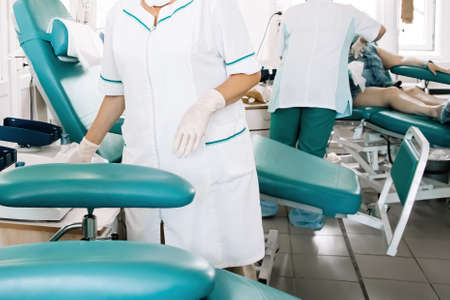 Nurse prepares chair for blood donors in medical laboratory. International Blood Donation Day. Equipment for blood transfusion in city blood bank.の写真素材