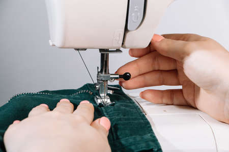 Woman designer or tailor working on sewing machine. Hands hold and sew on details of clothing. World tailors day. Close-up of sewing process.の写真素材