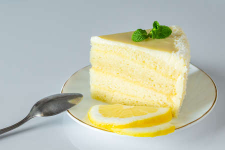 Piece of biscuit dessert  with lemon and coconut flakes. Layered vanilla cake on a white plate.の写真素材