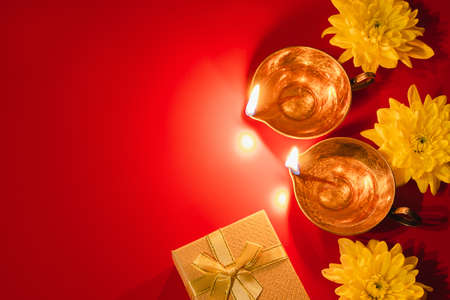 Happy Diwali. Diya oil lamp, flowers and gift boxes on red background. Celebrating the Indian...