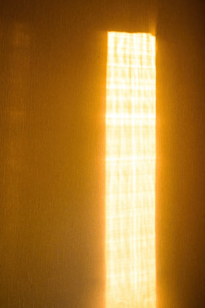 Sunbeam on yellow wall of house. Surface texture with sun glare. Abstract background. Vertical photo.の写真素材
