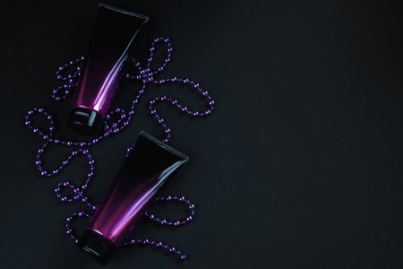 Stylish black and pink cosmetic tubes on dark background. Cosmetic bottles and purple decorations. Gift for winter holidays. Advertising product. Copy space.の写真素材