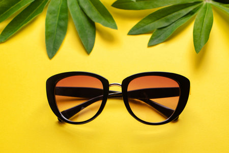 Sunglasses and green leaves on yellow background. Summer flatlay. Rest and vacation concept.の写真素材