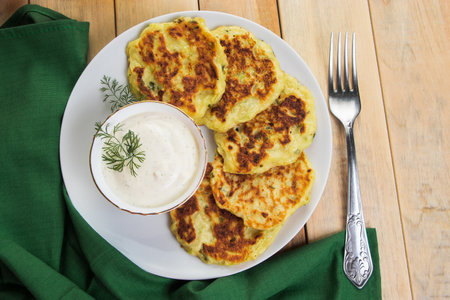 Vegan green zucchini pancakes in plate and creamy sauce. Healthy vegan diet food on wooden background. Top view.の写真素材