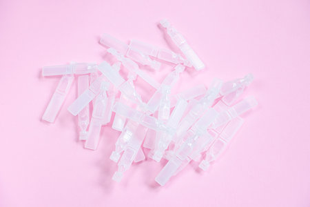 Medical eye drops in plastic pipettes on pink background. Pile of empty plastic ampoules for drops....