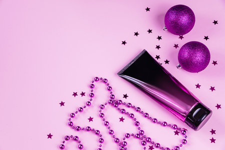 Stylish plastic bottle of cosmetics on pink background. Squeeze tube of skin care cream or lotion and Christmas decorations. Unbranded product for advertising. Holiday shopping and sales. Copy space.の写真素材