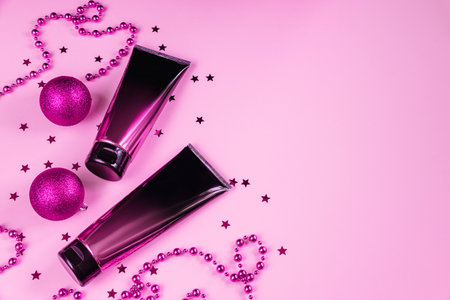 Set of black and pink squeeze cosmetic bottles and Christmas decorations on pastel background. Skin care cream in luxury cosmetic tube. Unbranded product for advertising and holiday sale. Copy spaceの写真素材