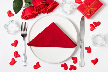 Table setting for valentine's day. Red roses and cutlery on white background.の写真素材