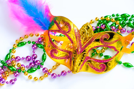 Golden carnival mask and colorful beads on white background. Closeup symbol of Mardi Gras or Fat Tuesday. Holiday decorations in gold, green and purple.の写真素材