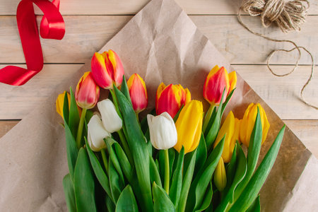 Woman florist ties red bow on large bouquet of colorful tulips. Fresh spring flowers on wooden background.の写真素材