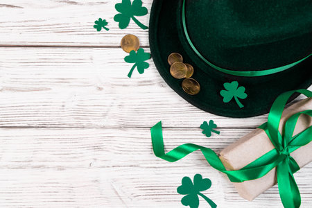 Background for St. Patrick's Day. Leprechaun hat, gold coins and clover shamrock on white wooden background. Good luck symbols. Place for text.の写真素材