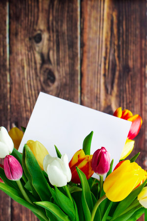 Colorful tulips bouquet and greeting card on wooden background. Holiday gift. Spring symbol, place for text.の写真素材