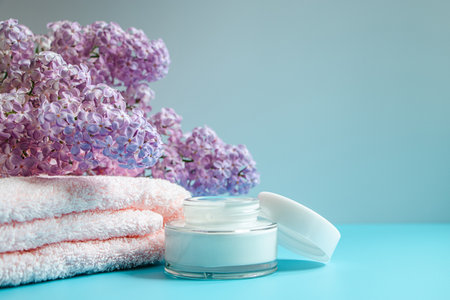 Spa and skin care concept. Towel, cream and soap on background of delicate lilac flowers.の写真素材