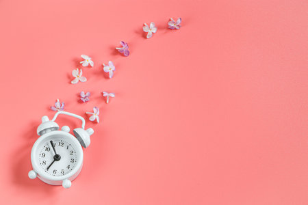 Small retro alarm clock and lilac flowers on pink background. Concept of spring and awakening of nature. Flatlay, copy space.の写真素材