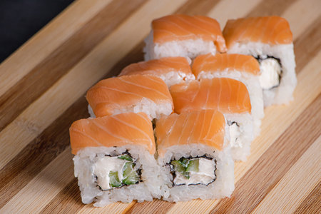 Philadelphia sushi roll on wooden bamboo tray on black background. Popular Asian dish of rice and salmon. Fast delivery of Japanese takeaway food.の写真素材