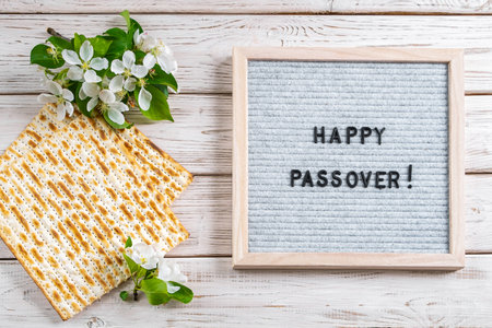 Happy Passover flatlay. Jewish matzo bread and flowers on white wooden background. Holiday greeting card. Copy space.の写真素材