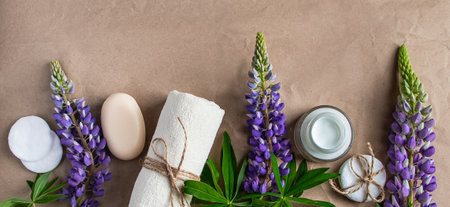 Natural organic cosmetics and lupine flowers on craft paper background. Moisturizing cream, soap and towel. Body care concept. Spa and beauty treatments, relaxation. Copy space, banner format.の写真素材