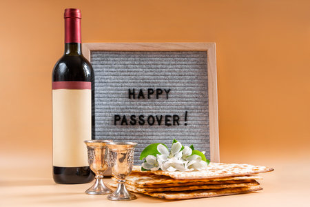 Jewish holiday Passover. Bottle of wine, spring flowers and matzah bread on beige background.