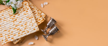 Happy Passover. Traditional Jewish holiday. Silver wine cups, spring flowers and matzo bread on beige background. Copy space, banner format.の写真素材