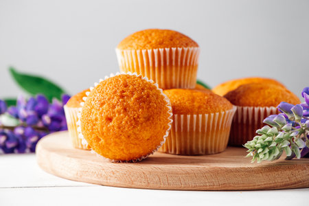 Soft fresh muffins on textile napkin. Delicious pastries and purple lupine flowers on white wooden background. Preparing dessert in confectionery.の写真素材
