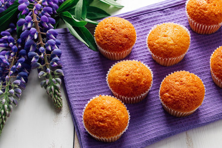 Freshly baked muffins and purple lupins on white wooden background. Homemade baking, preparing sweet dessert. Summer recipe.の写真素材