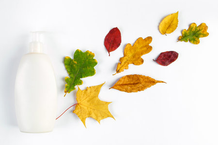White cosmetic bottle and autumn yellow leaves. Autumn skin care concept. Minimalistic design of eco-friendly cosmetics. Copy space.の写真素材