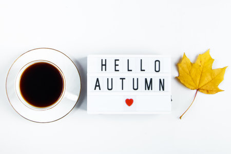 Hello autumn concept. Cup of coffee and sign with  inscription on white background. Fallen leaves and a hot drink.の写真素材