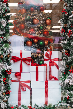 Gift boxes in store window. Season of Christmas shopping and sales. White boxes with red ribbons on background of Christmas decorations.の写真素材