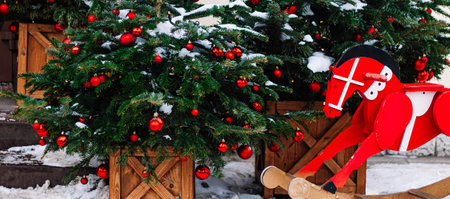 Christmas decorations on porch of house. Festive tree with red Christmas balls and wooden red horse. Holiday season, street decor. Banner format.の写真素材