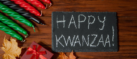 Kwanzaa African American holiday. Seven candles red, black and green on a natural wooden background. Symbols of African heritage. Congratulatory inscription and gifts.の写真素材