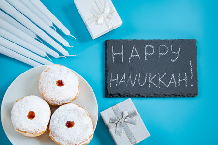 Happy Hanukkah. Jewish dessert sufganiyot donuts on blue background. Symbol of religious Judaism holiday. Inscription on the chalk board.の写真素材