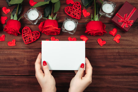 Female hands hold greeting card for valentine's day. Red roses and hearts on wooden background.の写真素材