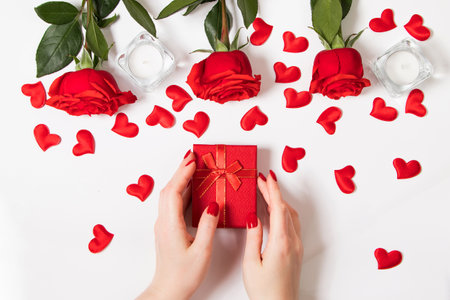 Female hands hold gift box for valentine's day. Red roses and candles on a white background.の写真素材