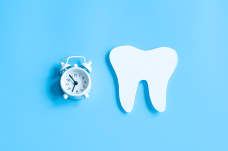 Paper cut mockup of tooth and alarm clock on blue background. Dental care concept. International Dentist Day. Greeting card for professional holiday.の写真素材