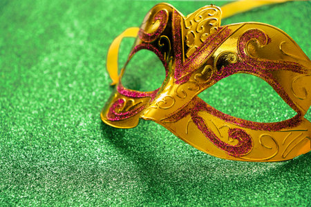 Golden carnival mask on green shiny background. Mardi Gras concept. Fat Tuesday symbol close-up. Greeting card, copy space.の写真素材