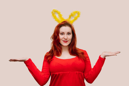 Young red-haired woman in red dress wearing easter costume with bunny ears. Easter concept, copy space. Studio portrait of smiling woman.の写真素材