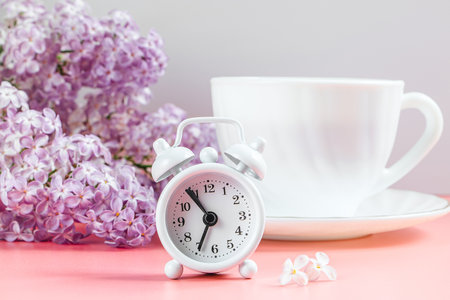 Alarm clock, lilac flowers and cup of coffee on light background. Spring and early morning concept.の写真素材