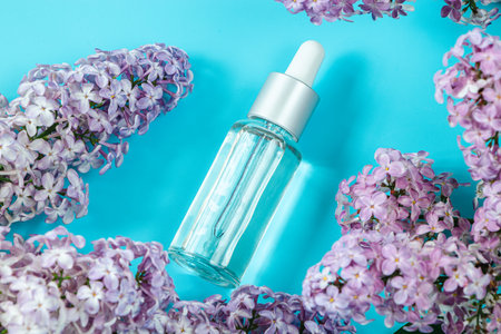 Skin care cosmetics on blue background. Moisturizing serum, cream and delicate lilac flowers. Spa and beauty treatment concept. Copy space.の写真素材