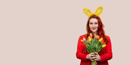 Young red-haired woman in red dress wearing bunny ears holding bouquet of tulips. Easter concept, copy space.の写真素材