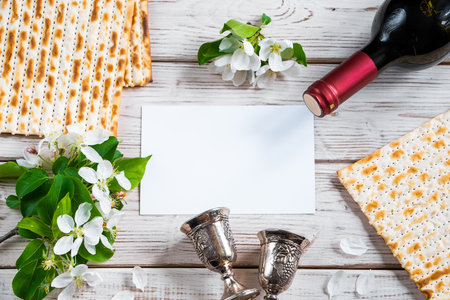 Celebrating Jewish religious holiday of Passover. Bottle of wine, matzo and flowers on white wooden background. Festive flatlay. Copy space.の写真素材