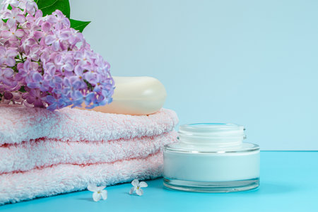 Spa and skin care concept. Towel, cream and soap on background of delicate lilac flowers.の写真素材