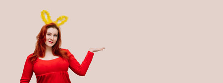 Young red-haired woman in red dress wearing easter costume with bunny ears. Easter concept, copy space. Studio portrait of smiling woman.の写真素材