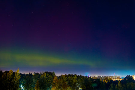 Northern lights over city. Pale light of Aurora borealis in night sky. Color flashes in northern hemisphere.の写真素材