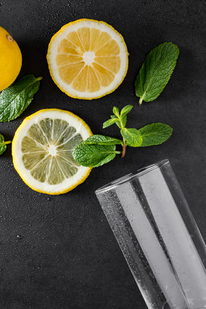 Fresh juicy lemon and mint leaves on black background. Ingredients for a summer cocktail. Food background. Advertising concept of refreshing drink. Vertical photo.の写真素材