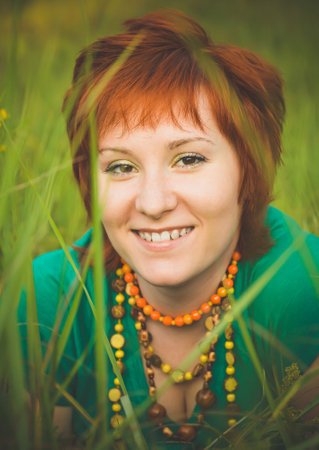 Young red-haired woman sitting in the grass and enjoying a sunny summer day. Portrait of a happy smiling young girl in nature.の写真素材