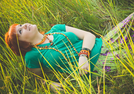 Young red-haired woman lying in the grass and enjoying a sunny summer day. Happy smiling young girl in nature.の写真素材
