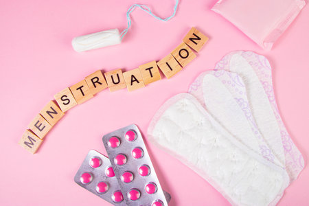 Sanitary pads, tampons, pills on pink background. Set of feminine hygiene products for menstruation. Womens health concept. Wooden lettering.の写真素材