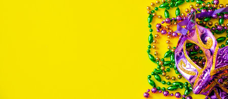 Carnival mask and colorful beads on yellow background. Mardi Gras or Fat Tuesday symbol. Holiday decorations in gold, green and purple. Copy space.の写真素材