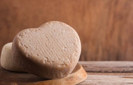 Cheese in the shape of a heart on a wooden table. Place for text.